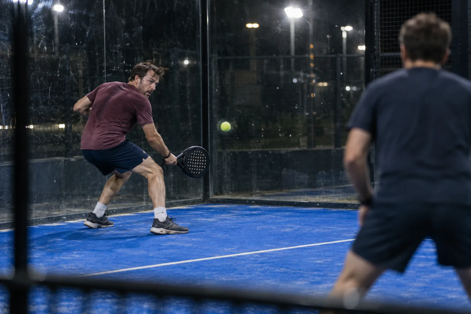 Two players on a blue padel court at night